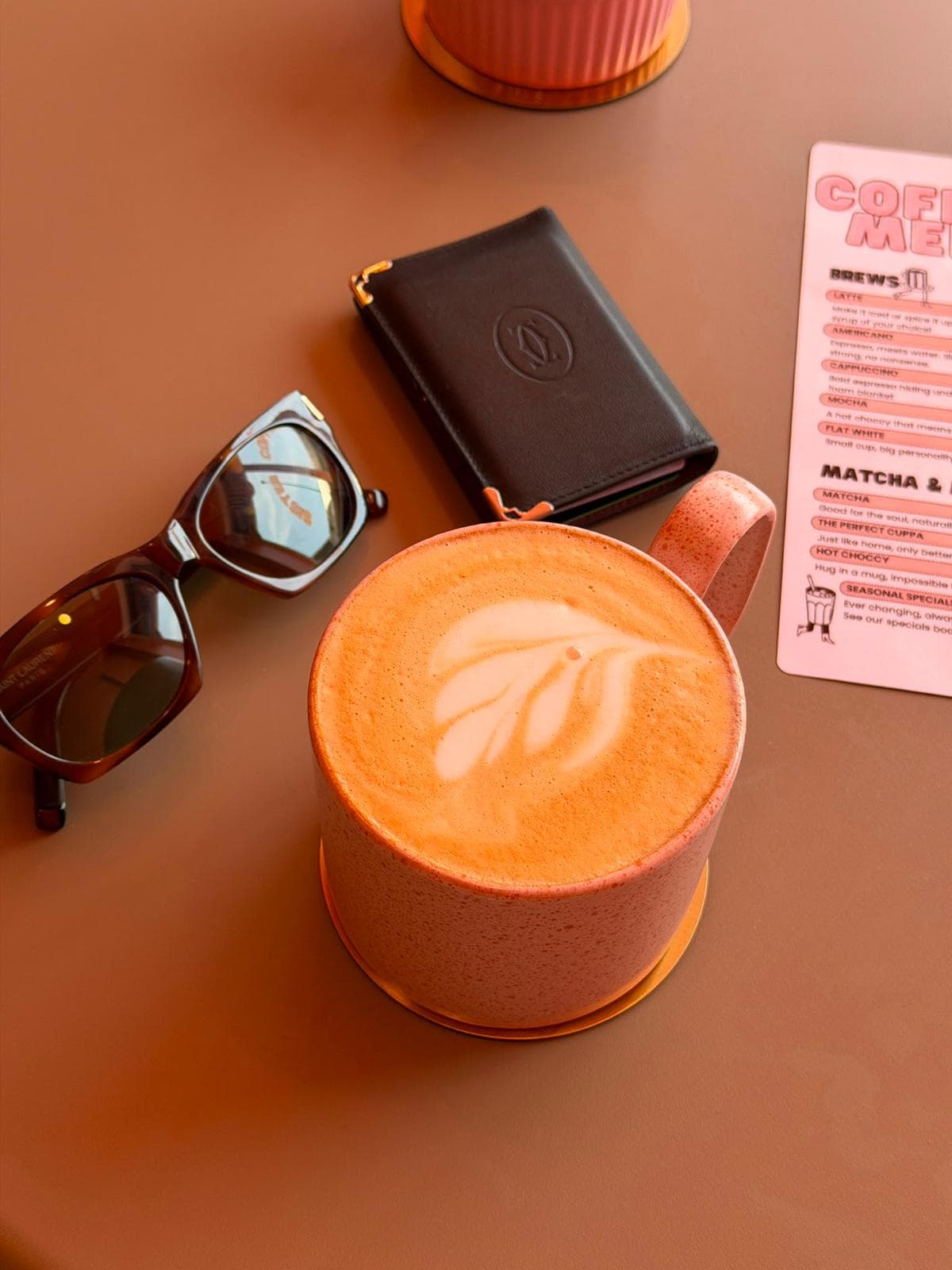 A latte with leaf art on a terracotta table next to the Sister Coffee menu card
