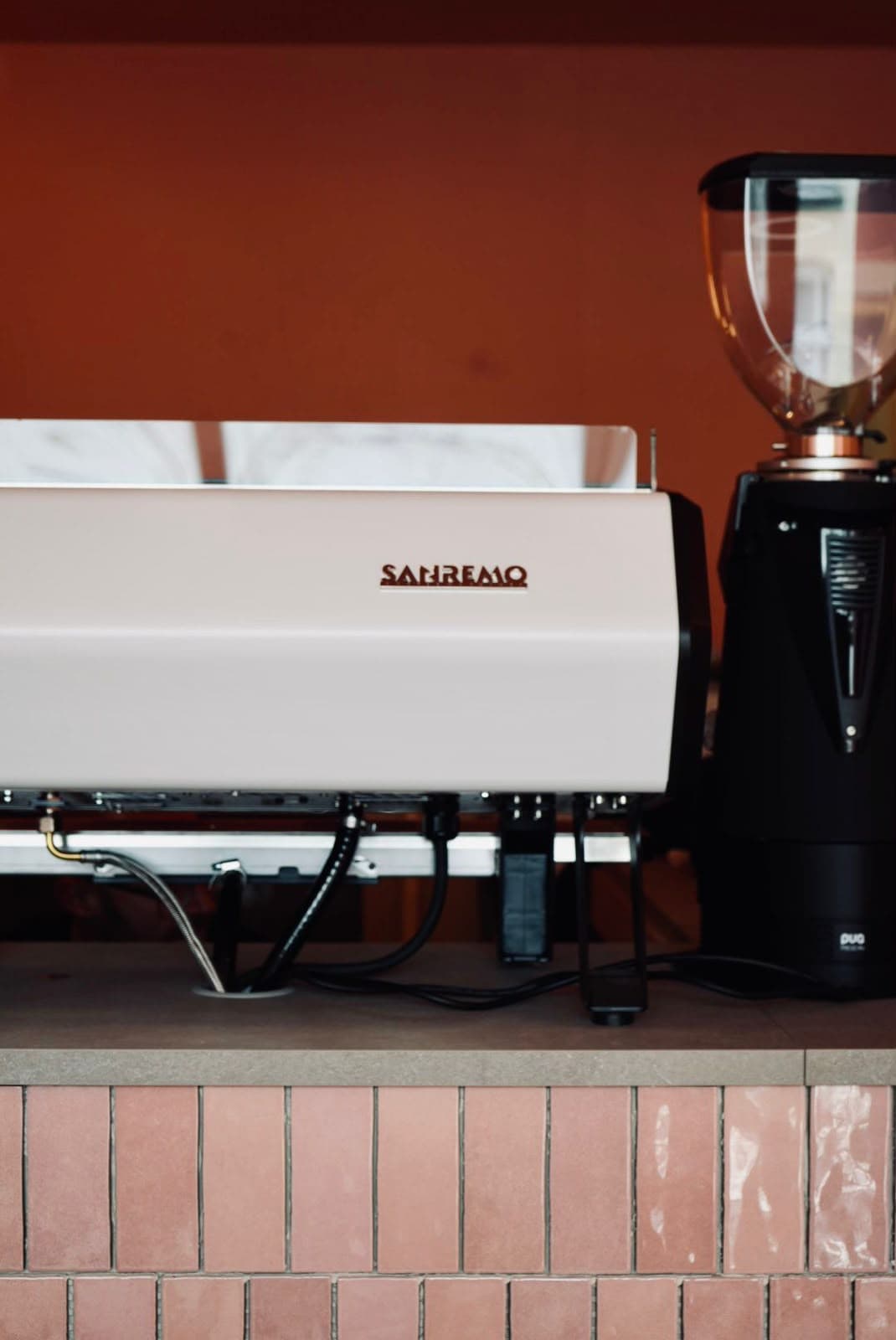 The white Sanremo espresso machine against a terracotta wall