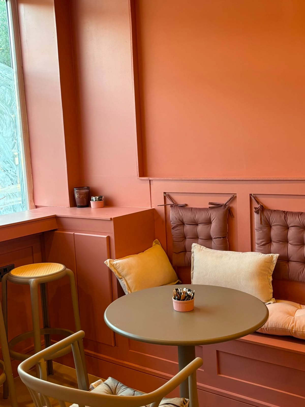A window table with cushioned bench seating in terracotta and blush