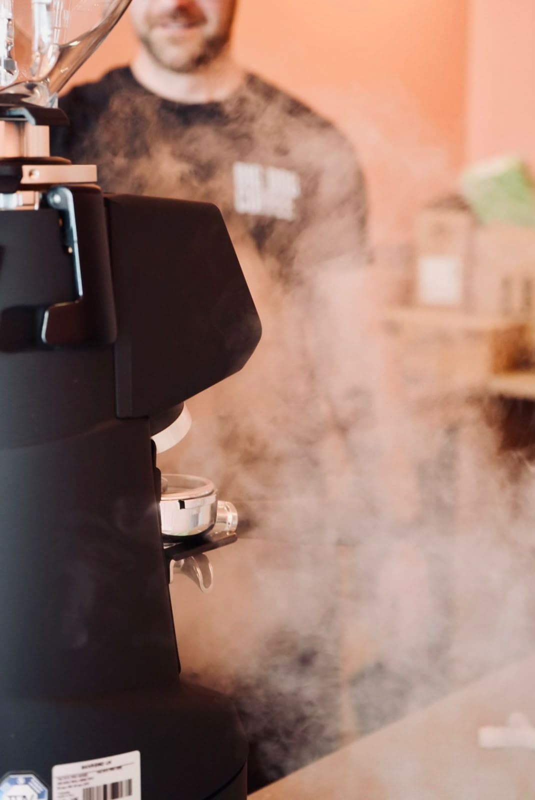 Steam rising from the grinder as a barista works behind it